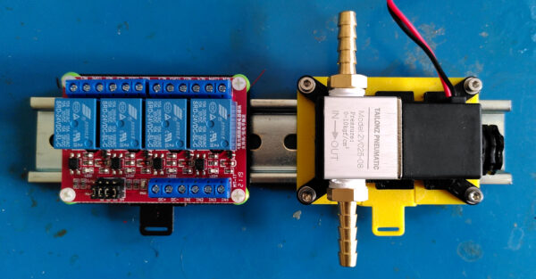 Physical DIN rail clip mounts holding a relay and solenoid on a metal DIN rail